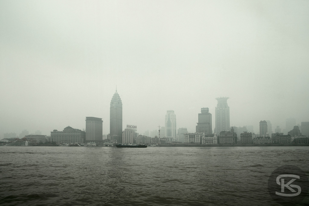 Shanghai 2008: Historische Skyline des Bunds mit Zollamt-Glockenturm im Nebel | Eine historische Aufnahme der Skyline des Bunds (Puxi-Viertel) in Shanghai (China), aufgenommen aus der Perspektive von Pudong im Jahr 2008. Das Bild zeigt die ikonischen Gebäude im Kolonialstil, darunter das markante Zollamt mit seinem Glockenturm, eingetaucht in dichten Nebel oder Smog über dem Huangpu-Fluss. - Realisiert mit Pictrs.com