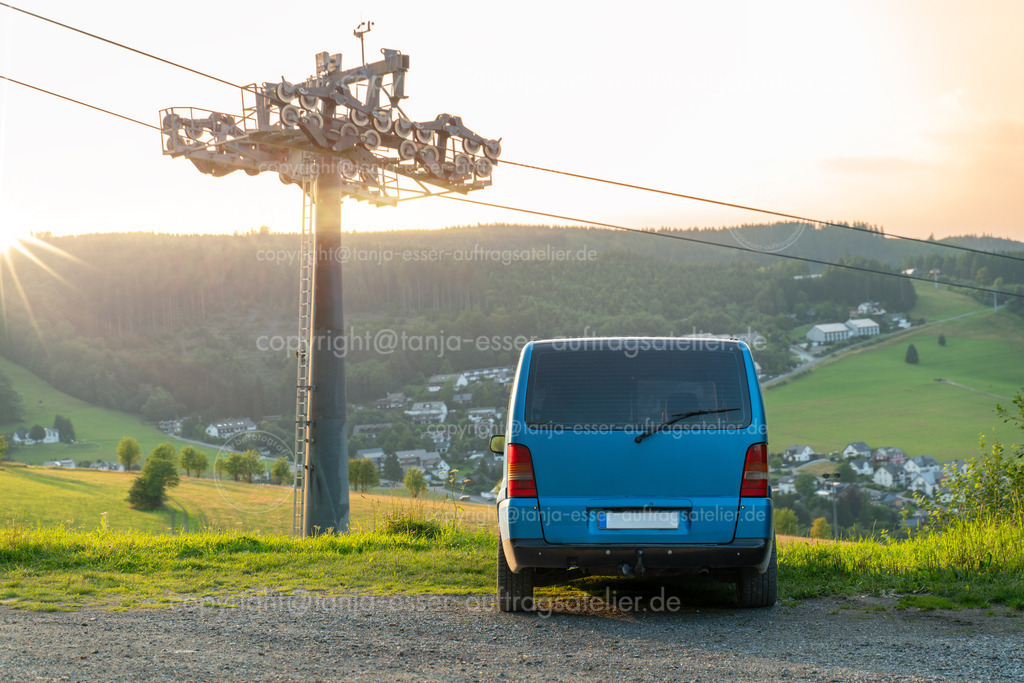 Vanlife Willingen D | Vanlife. Der Van parkt mit der Rückseite sichtbar vor einer schönen Aussicht in Willingen Upland in Deutschland. Neben dem Fahrzeug ist ein Skilift. Stimmungsvolle Aufnahme mit Sonnenuntergang. 