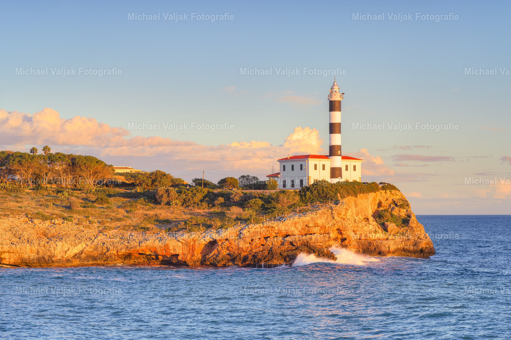 Leuchtturm von Portocolom auf Mallorca | Der Leuchtturm von Portocolom rückt in dieser Aufnahme eindrucksvoll in den Mittelpunkt. Im letzten Licht der untergehenden Sonne beginnt seine Fassade warm zu glühen, während die Farben des Abends langsam weicher werden. Ein stiller, intensiver Moment, der die Ruhe der mallorquinischen Küste perfekt einfängt. - Realisiert mit Pictrs.com