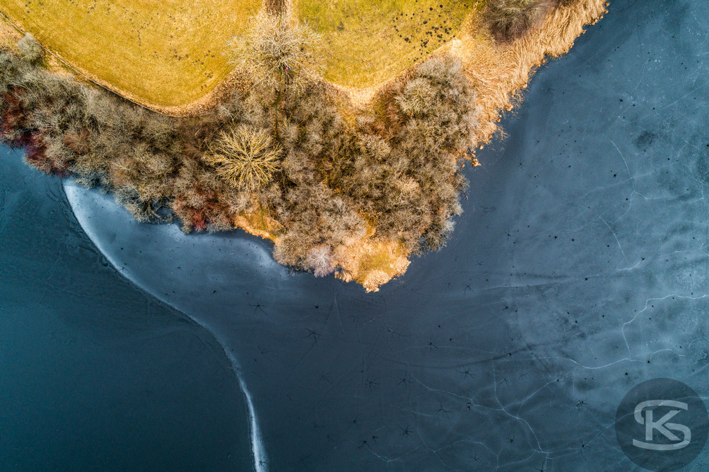 Zugefrorener See im Allgäu – Drohnenaufnahme von Eisstrukturen am Ufer | Beeindruckende Luftaufnahme eines vollständig zugefrorenen Sees im Allgäu. Die Drohnenfotografie zeigt faszinierende Eisstrukturen, Uferbereiche und natürliche Wintermuster aus der Vogelperspektive – einzigartige Winterlandschaft von oben. - Realisiert mit Pictrs.com