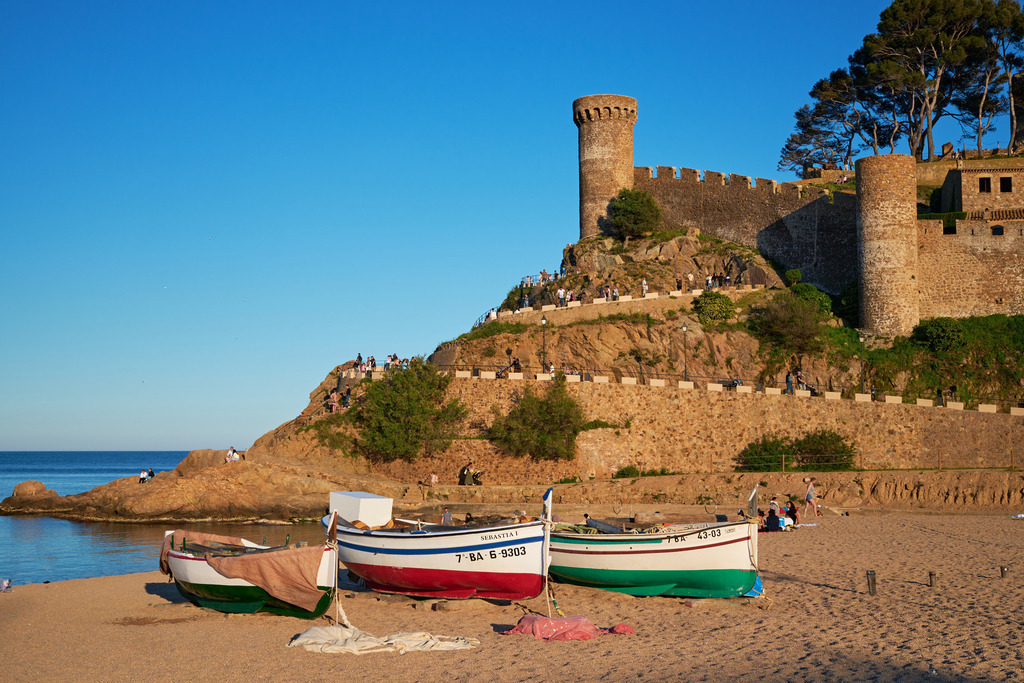Blick über den Strand auf die Vila Vella | Tossa de Mare, Frankreich - May 11, 2024: Blick über den Strand auf die Vila Vella mit blauem Himmel und Booten im Vordergrund. - Realisiert mit Pictrs.com