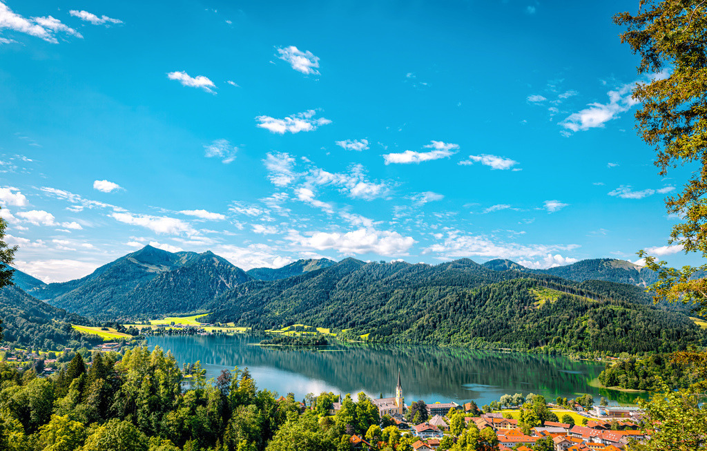 Malerischer Panoramablick auf den den Schliersee,Miesbach in Oberbayern | Das Bild zeigt einen malerischen Panoramablick auf den Schliersee im bayerischen Mangfallgebirge.Lage: Der See befindet sich im Landkreis Miesbach in Oberbayern.Landschaft: Er ist von bewaldeten Hügeln und Bergen der bayerischen Voralpen umgeben.Ansicht: Im Vordergrund sind das Ufer des Ortes Schliersee und ein markanter Kirchturm zu erkennen - Realisiert mit Pictrs.com