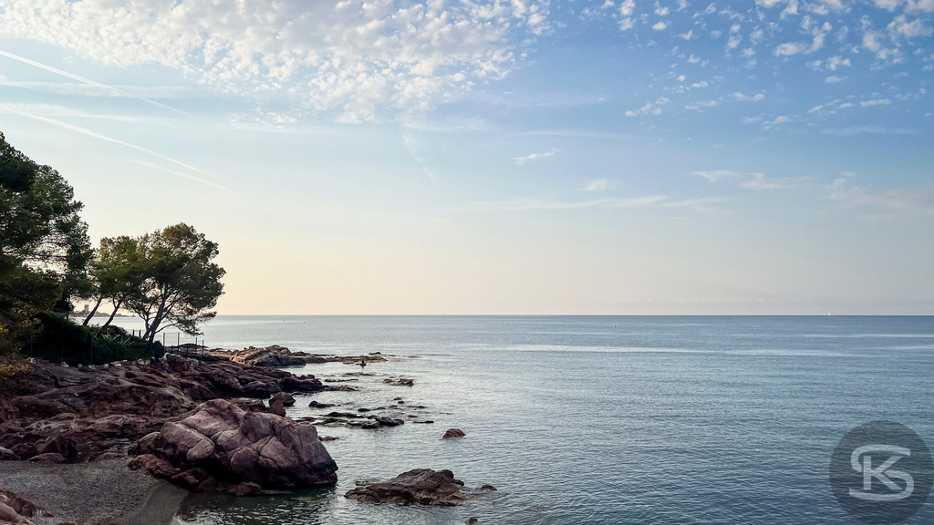 Sonnenaufgang über dem Mittelmeer – Morgenstimmung an der Côte d’Azur | Stille Küstenlandschaft an der Côte d’Azur bei Sonnenaufgang: Rote Felsklippen und Pinien am Ufer des ruhig spiegelnden Mittelmeers unter einem zart bewölkten Morgenhimmel. - Realisiert mit Pictrs.com