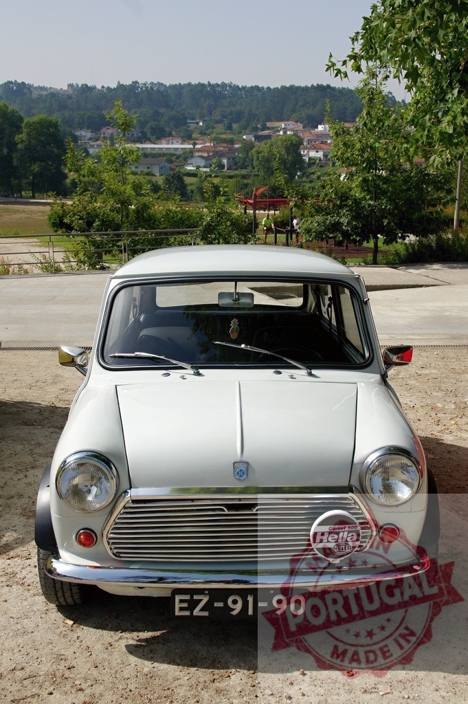 Classic Mini Cooper parked with scenic background, showcasing vintage charm | White Mini Cooper parked, exuding vintage charm against a backdrop of a picturesque town - Realized with Pictrs.com