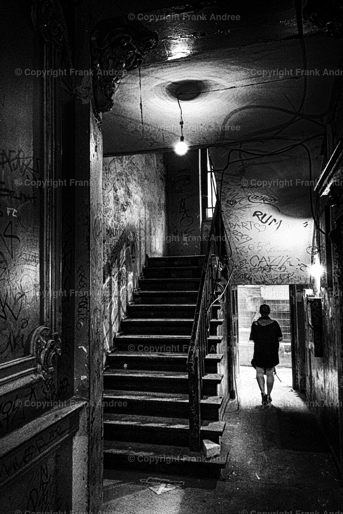Treppenhaus Berlin Prenzlauer Berg | Eine Frau geht aus einem unsanierten Treppenhaus in Berlin Prenzlauer Berg. Straßenfotografie aus Berlin in schwarz und weiß. - Realisiert mit Pictrs.com