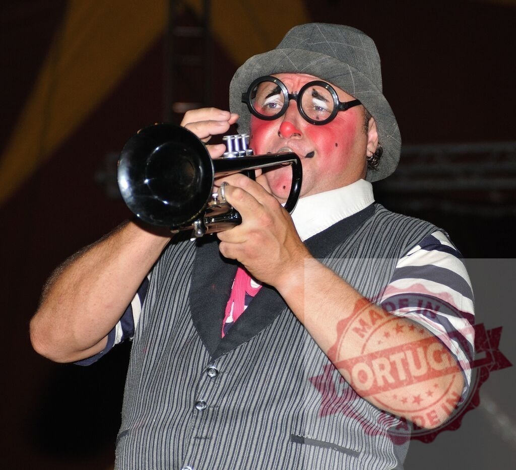 Clown performer playing trumpet bringing circus entertainment | Clown with makeup and costume playing a brass trumpet in a circus tent - Realized with Pictrs.com