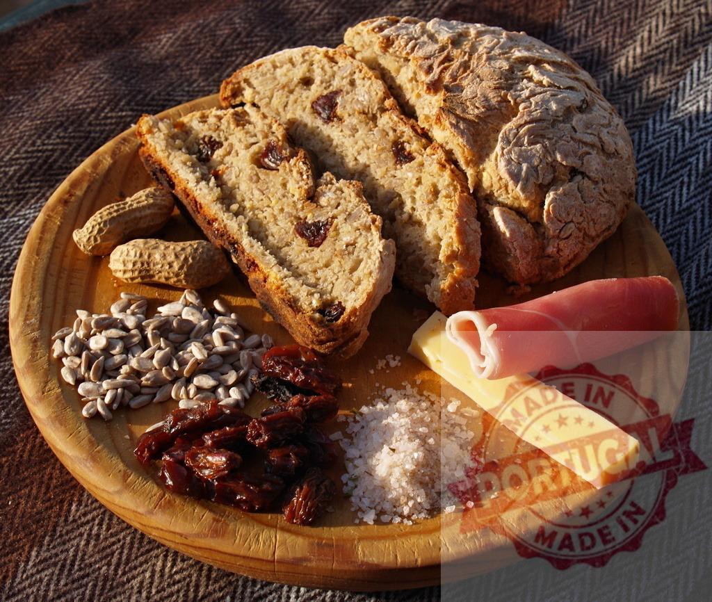 Rustic picnic bread with cheese, ham, nuts, and dried fruit | Rustic wooden plate holding sliced bread, cheese, ham, peanuts, sunflower seeds, raisins, and salt - Realisiert mit Pictrs.com