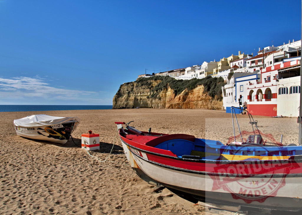 Traditional fishing boats resting on a beach in Algarve | Fishing boats beached on sand with a village and cliffs in the background - Realized with Pictrs.com