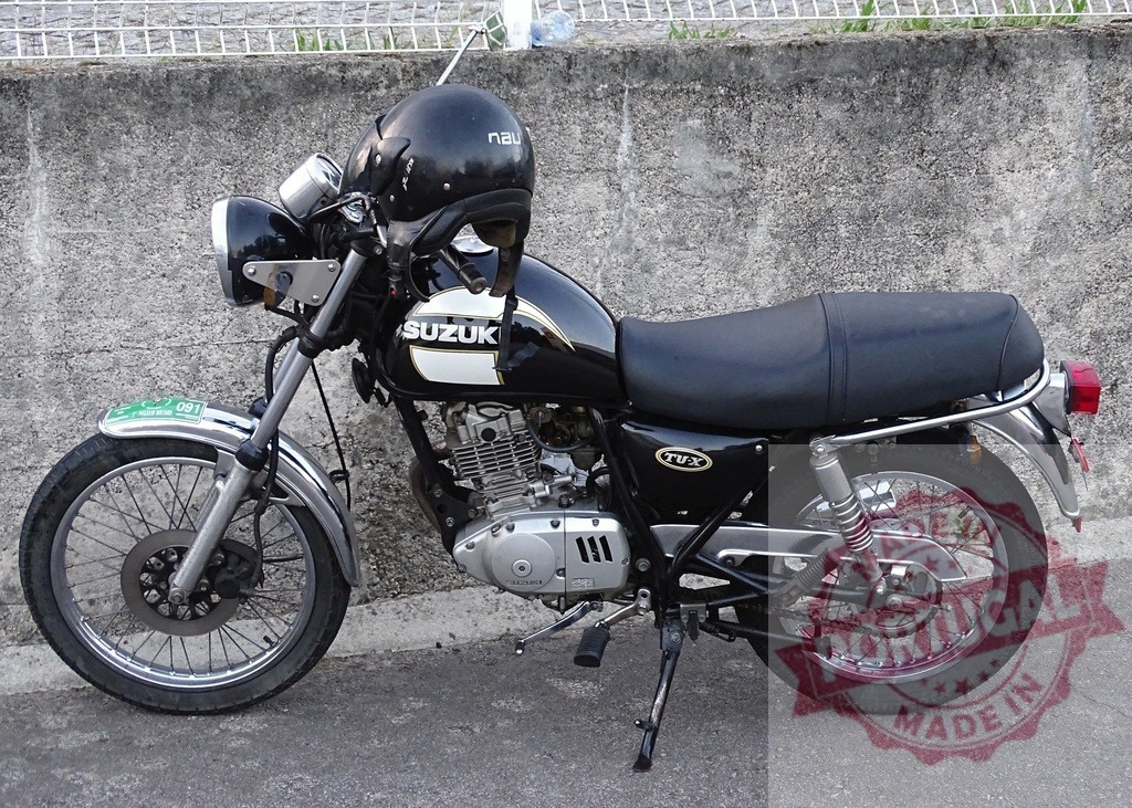 Black Suzuki TUX motorcycle parked with helmet resting on the fuel tank | Classic black Suzuki TUX motorcycle parked on the side of a road, with a helmet resting on the fuel tank - Realized with Pictrs.com