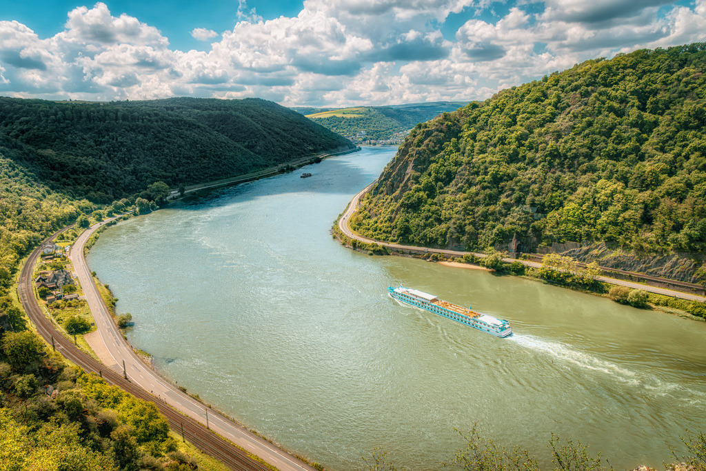 Blick auf den Rhein UNESCO-Welterbe Oberes Mittelrheintal,Flussschiff | Das Bild zeigt den Rhein im UNESCO-Welterbe Oberes Mittelrheintal mit einem Flussschiff auf Höhe der Loreley-Passage.Entlang des Stroms verlaufen die bewaldeten Schieferhänge, Uferstraßen und Eisenbahnlinien, die für diese Kulturlandschaft typisch sind.Der Abschnitt gehört zu den bekanntesten touristischen und landschaftlichen Highlights des romantischen Mittelrheins zwischen Koblenz und Bingen - Realisiert mit Pictrs.com