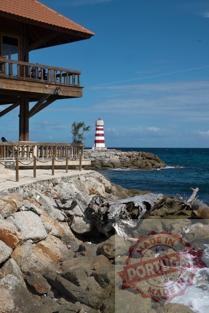 Bayahibe lighthouse on rocky shore with ocean view | Wooden building on rocks overlooking the red and white striped lighthouse and Caribbean Sea - Realized with Pictrs.com