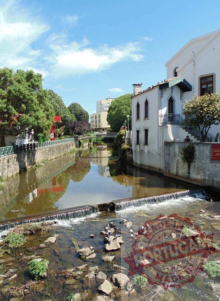 Aveiro Region - Portugal Aveiro urban canal with historical building and waterfall | Urban canal flowing past traditional architecture and lush trees under a blue sky in Portugal - Realisiert mit Pictrs.com