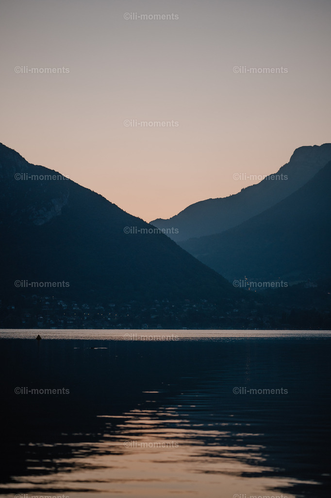 Morgendämmerung | „Die Morgendämmerung“ ist eine stimmungsvolle Naturaufnahme, die die besondere Magie des Moments kurz vor Sonnenaufgang einfängt. Hinter den majestichem Bergsilhouetten zeichnet sich bereits das zarte, erste Licht der Sonne ab – ein sanfter Schimmer, der den Beginn eines neuen Tages erahnen lässt. Der glitzernde See im Vordergrund reflektiert das feine Morgenlicht und verleiht der Szenerie eine ruhige, fast poetische Stimmung.Dieses Foto verbindet Minimalismus mit kraftvoller Atmosphäre und eignet sich ideal für Räume, in denen Ruhe, Achtsamkeit und natürliche Eleganz im Mittelpunkt stehen – sei es im Wohnzimmer, Büro, Schlafzimmer, Spa oder Hotelbereich. - Realisiert mit Pictrs.com