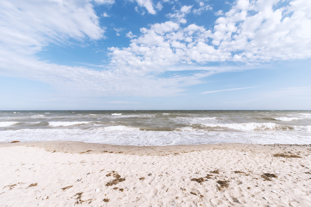 Wandbild: Strandweite in Schönhagen | Der Strand in Schönhagen zeigt sich mit dynamischen Wellen, die kraftvoll über den hellen Sand laufen. Einzelne Tangspuren liegen am Ufer, während die Ostsee in stetiger Bewegung steht und der Himmel mit hellen Wolken die Szene nach oben öffnet. Die klare Horizontlinie und das Zusammenspiel aus lebendigem Wasser und weitem Himmel verleihen dem Motiv eine frische, maritime Energie. Dieses Wandbild bringt die natürliche Dynamik und die offene Küstenatmosphäre der Schönhagener Ostsee direkt in den Raum.