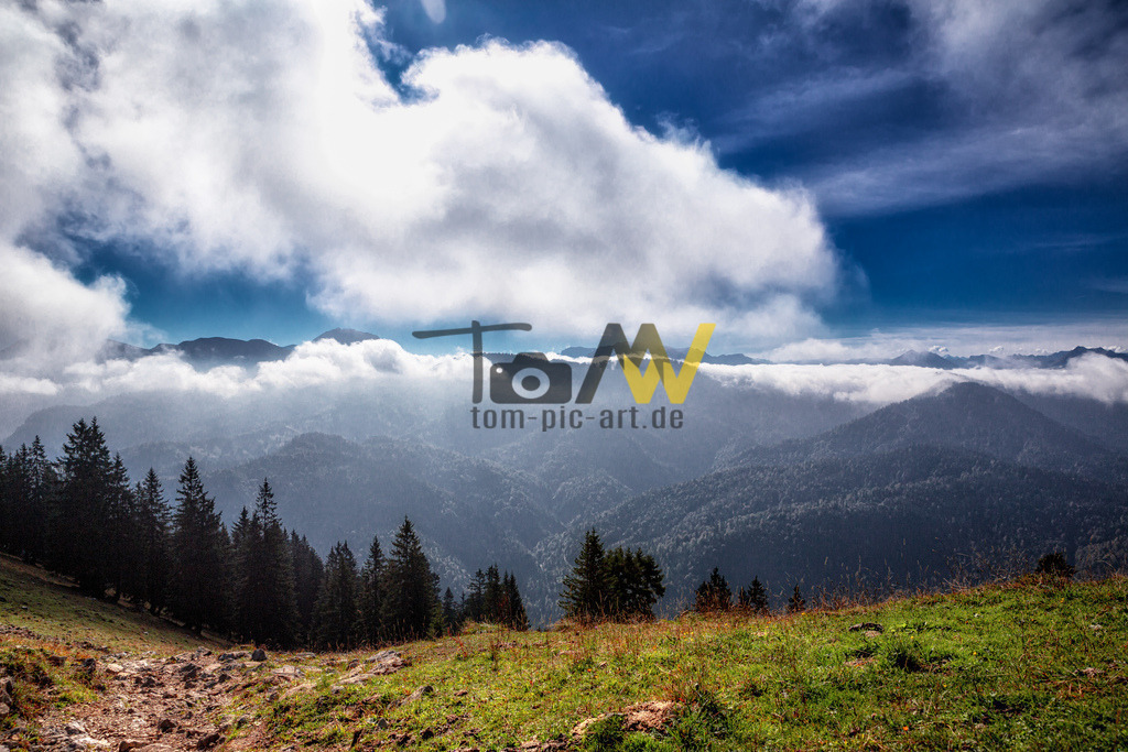 Fantastischer Blick über die Tegernseer Berge | Das Bild zeigt eine malerische Berglandschaft mit Nebelschwaden in den Tälern.Die Szenerie fängt die mystische Stimmung ein, die entsteht, wenn Berge im Nebel versinken. Nebel in Tälern, auch Kaltluftabfluss genannt, entsteht, wenn kühlere Luft absinkt und die Luftfeuchtigkeit den Taupunkt erreicht. Dieses Wetterphänomen tritt häufig bei Hochdruckwetterlagen im Winter auf, was zu einer sogenannten Inversionswetterlage führen kann.  - Realisiert mit Pictrs.com