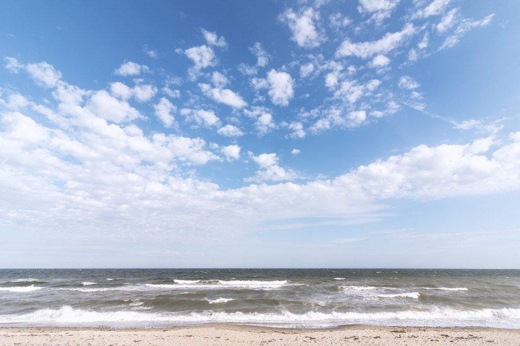 Wandbild: Sanfte Brandung am Strand von Schönhagen | Der Strand in Schönhagen zeigt sich hier in seiner sanften Ruhe: leichte Wellen rollen über den hellen Sand, die Ostsee wirkt weit und klar, und über dem Horizont ziehen helle Wolken durch den blauen Himmel. Das Motiv fängt die natürliche, entspannte Küstenatmosphäre ein und bringt die stille Weite der Schönhagener Ostseeküste als Wandbild direkt in den Raum.