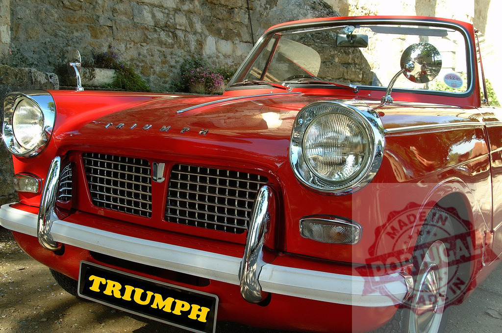 Red Triumph Herald Convertible parked near stone wall | Classic red Triumph Herald convertible car parked near a stone wall, enjoying the sunlight - Realized with Pictrs.com