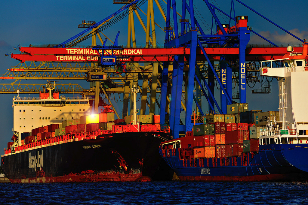 Containerschiff an der Brücke | Containerschiff beim Verladen an der Brücke mit goldenem Container - Realisiert mit Pictrs.com