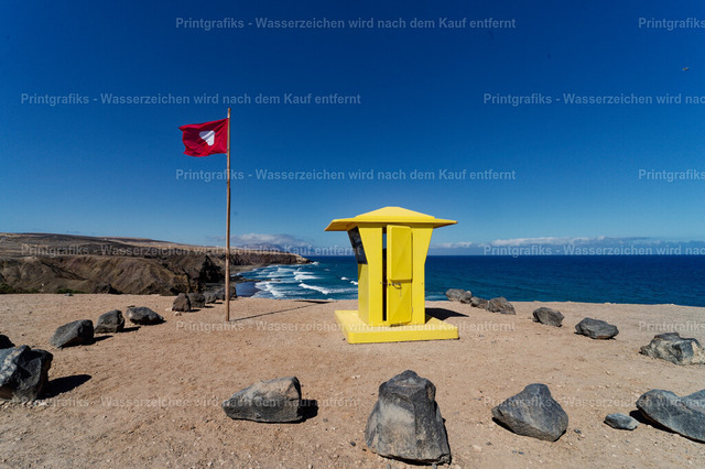 Gelber Strandturm auf Fuerteventura | Minimalistische Küstenszene auf Fuerteventura mit gelbem Strandturm, roter Fahne und tiefblauem Atlantik. Die klaren Farben, die karge Landschaft und der weite Himmel vermitteln sommerliche Ruhe und das Gefühl von Freiheit am Meer. - Realisiert mit Pictrs.com