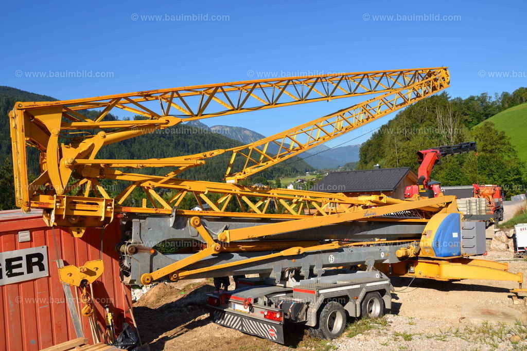 Kranaufbau | Platzierung Baukran auf vorbereitetem Kranstellplatz, gelber Kran auf Kranachsen, blauer Himmel wolkenlos