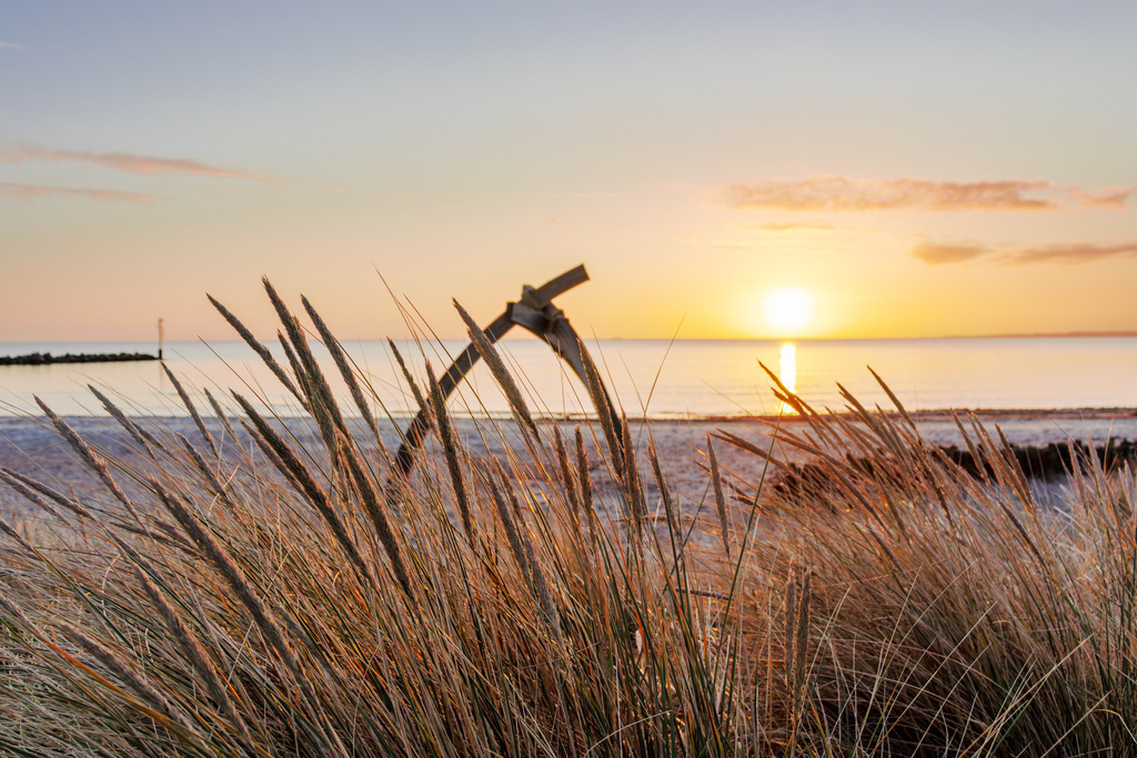 Wandbild: Magischer Sonnenaufgang am Strand in Damp | Sanfte Farben, beruhigende Naturmotive und die friedliche Weite des Meeres – dieses Wandbild strahlt Harmonie und Entspannung aus. Die aufgehende Sonne über der Ostsee taucht den Himmel in warmes Orange, während sich der Strandhafer sanft im Morgenlicht bewegt. Mit seinem weichen Farbspiel und der maritimen Ruhe fördert das Bild das Wohlbefinden und schafft eine angenehme Raumwirkung - Realisiert mit Pictrs.com