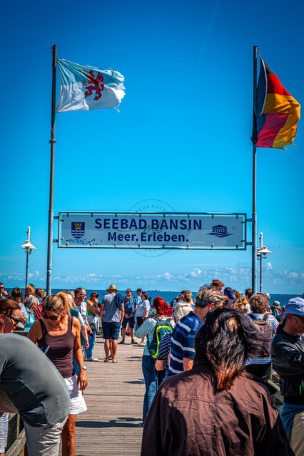 2026-08-08_11-55-20_020 | Menschenmenge am Seebad Bansin, flankiert von Flaggen unter blauem Himmel, genießt den Tag, Bansin, Usedom, Mecklenburg-Vorpommern, Deutschland - Realisiert mit Pictrs.com
