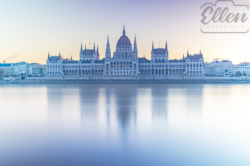 Blue Serenity | In the cool calm of early morning, the Hungarian Parliament is mirrored in the soft blue tones of the Danube. Light and water blend into a tranquil harmony, capturing the city’s quiet awakening. - Realisiert mit Pictrs.com
