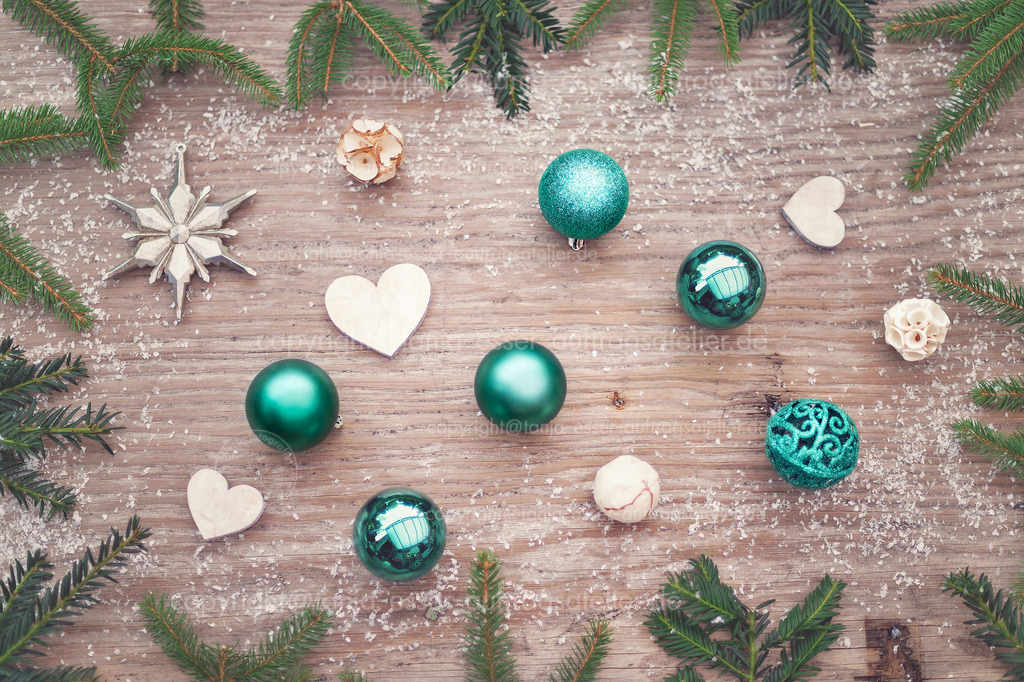 Christmas decoration in modern colors | Weihnachtliches Tannengrün umrahmt einen alten Echtholz-Hintergrund. Weihnachtskugeln in der aktuellen Farbe Türkis und Holzherzen sind verstreut und von oben fotografiert.
