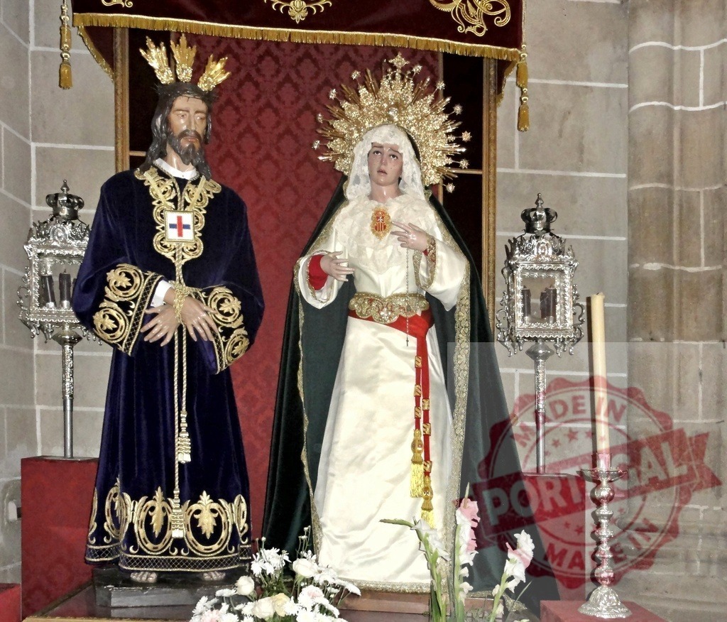 Religious wooden statues depicting Jesus Christ and Virgin Mary standing in a church | Two wooden statues of Jesus and Virgin Mary wearing elegant clothes and crowns, standing in a church near two candlesticks - Realized with Pictrs.com