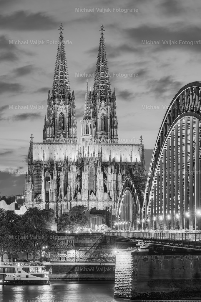 Beleuchteter Kölner Dom schwarz-weiß | Der Kölner Dom, ein Meisterwerk gotischer Architektur, erstrahlt auch in Schwarz-Weiß-Fotografien in beeindruckender Pracht. Die Beleuchtung hebt die filigranen Details der Fassade hervor und lässt die mächtigen Türme noch imposanter wirken. Besonders nachts, wenn die Lichter die Dunkelheit durchbrechen, wird die majestätische Statur des Doms betont, was bei Schwarz-Weiß-Aufnahmen zu einem dramatischen und zeitlosen Effekt führt. Diese Art der Fotografie fängt die Essenz des Doms auf eine Weise ein, die Farbbilder nicht können, und bietet einen einzigartigen Blick auf dieses historische Wahrzeichen. - Realisiert mit Pictrs.com