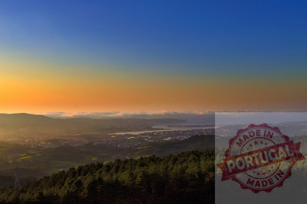 Colorful sunrise over city and sea of fog covering valley and hills with forest in foreground | Aerial view of a valley and a city covered by fog during a colorful sunrise with forest and hills in foreground - Realized with Pictrs.com
