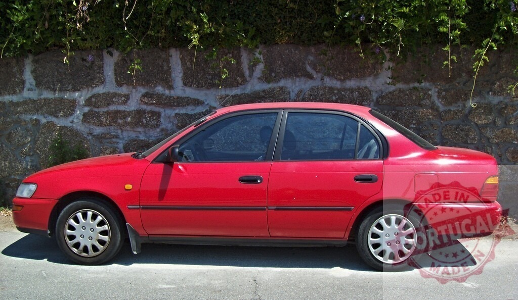 Red Toyota Corolla sedan parked by stone wall | Red Toyota Corolla sedan parked alongside an old stone wall with green vegetation - Realized with Pictrs.com