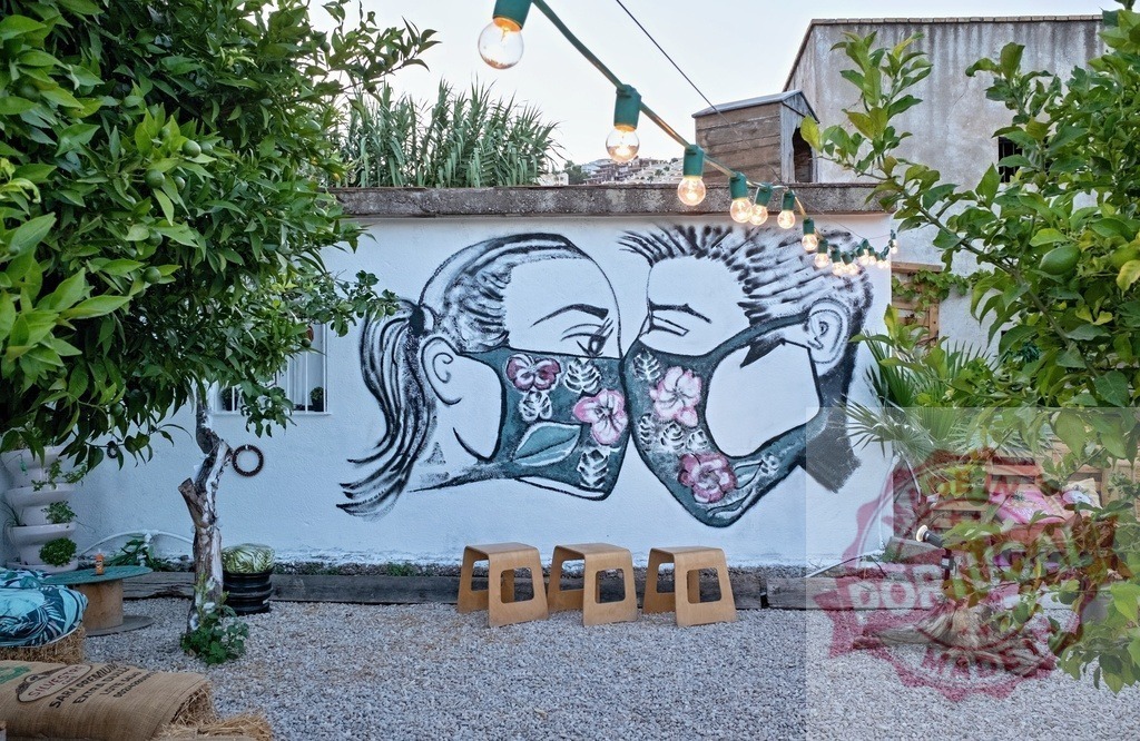 Street art mural showing a couple kissing with face masks in an outdoor patio | Romantic street art mural of kissing couple wearing face masks during pandemic - Realisiert mit Pictrs.com