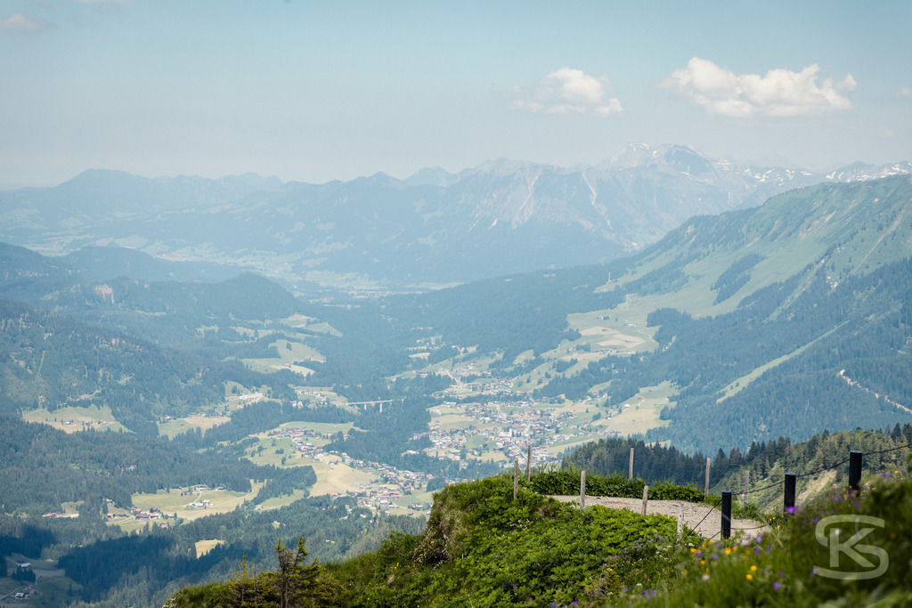 Blick vom Walmendinger Horn Richtung Nebelhorn - Kleinwalsertal Panorama | Weitläufiges Alpenpanorama vom Walmendinger Horn mit Blick Richtung Nebelhorn und ins Kleinwalsertal. Beeindruckende Aussicht über Täler, Almwiesen, Bergdörfer und majestätische Gipfel der Allgäuer Alpen unter dunstiger Sommersonne. - Realisiert mit Pictrs.com