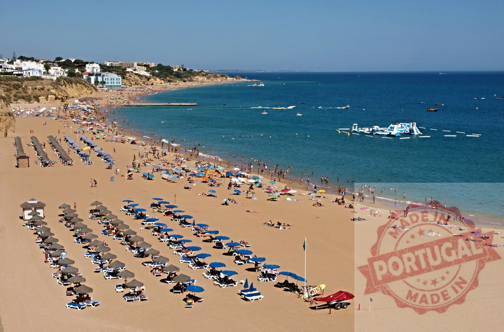 Praia dos Pescadores beach with crowded people in Albufeira, Portugal | Crowded beach with tourists, sunbeds, umbrellas, and a water park under a clear sky - Realized with Pictrs.com