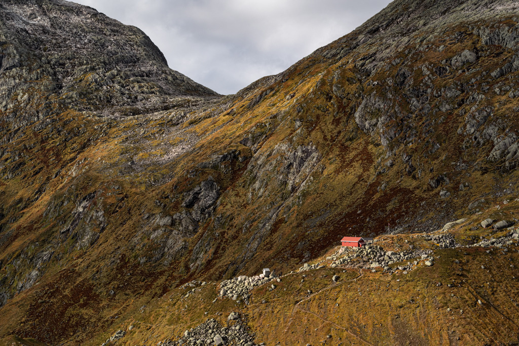 Selbstversorgerhütte Flatbrehytta umgeben von rauher Berglandschaft im Herbst 2021. | Die von der Sonne bestrahlte Hütte Flatbrehytta steht einsam vor schroffen Berghängen und die umgebenden Flechten und Gräser erstrahlen in herbstlichen Farbtönen. - Realisiert mit Pictrs.com