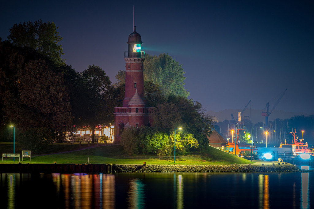 Leuchtturm Holtenau | Eine beeindruckende Nachtaufnahme des Leuchtturms Holtenau. Das Licht des Leuchtturms erzeugt einen hellen, sichtbaren Lichtstrahl, der sich in der Dunkelheit des Nachthimmels abzeichnet. Die Struktur des Turms ist im Kontrast zur Dunkelheit des Himmels und des umliegenden Geländes gut erkennbar. Das Leuchtfeuer des Holtenau-Leuchtturms weist Schiffen den sicheren Weg durch die Nacht und ist ein Zeichen der Hoffnung und des Schutzes in einer dunklen Umgebung. Es ist ein wundervolles Beispiel für die maritime Architektur und die Rolle, die Leuchttürme in der Geschichte der Seefahrt spielen.