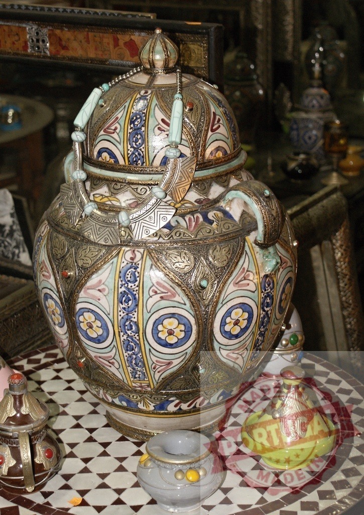 Moroccan pottery jar with ornate metalwork and turquoise necklace | Elaborate Moroccan handcrafted jar featuring intricate patterns and a silver necklace on a mosaic table - Realized with Pictrs.com