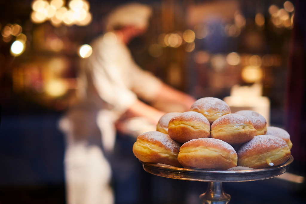 Faschingskrapfen in der Auslage der K. u. K. Hofzuckerbäckerei Demel | Wien, Austria - November 22, 2021: Faschingskrapfen in der Auslage der K. u. K. Hofzuckerbäckerei Demel, im Hintergrund ein Bäcker. - Realisiert mit Pictrs.com