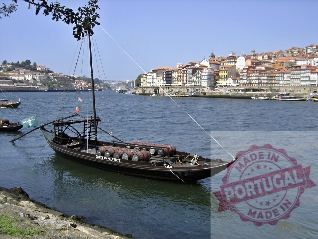 Rabelo boat carrying wine barrels on Douro River in Porto. Porto - Portugal | Rabelo boat floating on the Douro River with historic Ribeira buildings in the background - Realized with Pictrs.com