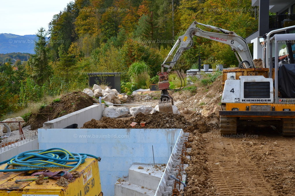 Steinschlichtung | Bagger beim Versetzen von Kalksteinen für Stützmauer neben Pool