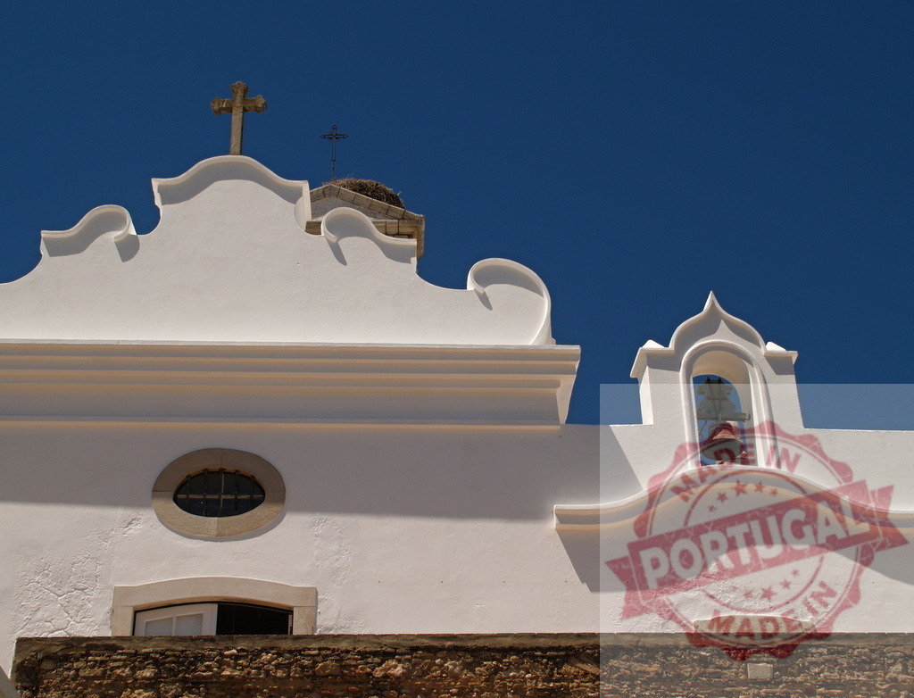 Traditional whitewashed church facade with bell and cross under blue sky | Whitewashed architecture of a historic church featuring an ancient bell and Christian cross against a clear blue sky - Realized with Pictrs.com