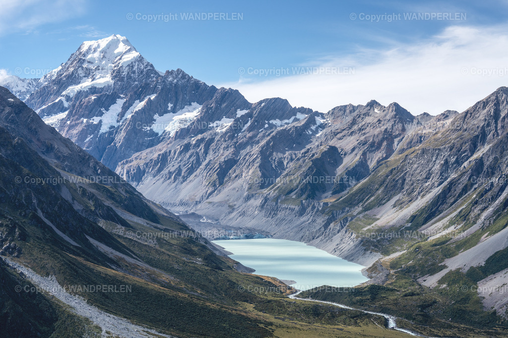 Mount Cook | Ein atemberaubendes Luftbild zeigt den majestätischen Aoraki / Mount Cook, Neuseelands höchsten Berg, der scharf gegen einen klaren blauen Himmel aufragt. Darunter liegt ein türkisfarbener Gletschersee in einer tiefen Schlucht, flankiert von steilen, felsigen Hängen. Die Szene betont die raue Schönheit der Südlichen Alpen, mit schneebedeckten Kanten, freiliegenden Felsen und Gletschermoränen. Das Bild wurde von einer erhöhten Position aus aufgenommen, um einen weiten Blick auf diese ikonische Alpenlandschaft zu ermöglichen. - Realisiert mit Pictrs.com