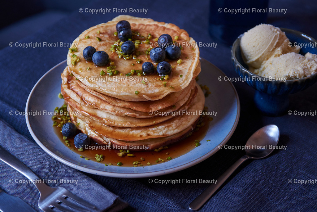 Pancakes mit Blaubeeren und Ahornsirup | gestapeltet Pancakes mit Blaubeeren, Ahornsirup und Pistazien mit Vanilleeis auf dunkler Tischdecke - Realized with Pictrs.com