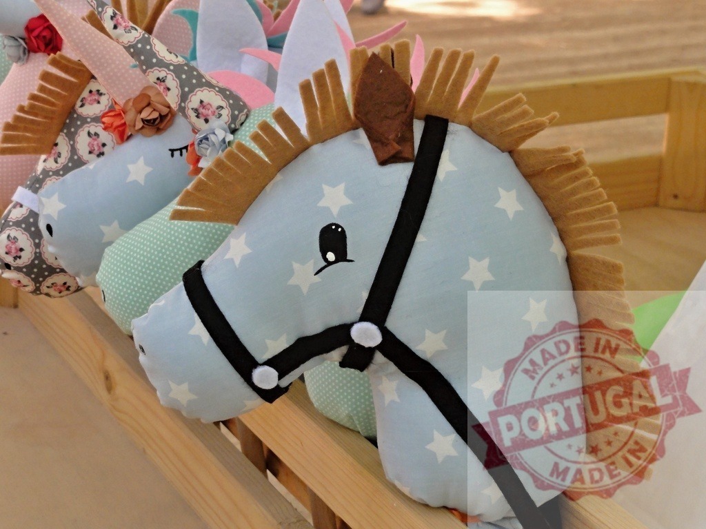 Plush hobby horse toys handmade for children playing | Handmade plush horse and unicorn toys lined up in a wooden stall for imaginative play - Realized with Pictrs.com