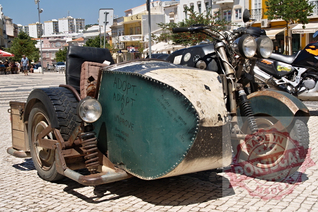 Custom motorcycle and sidecar parked on urban square | Unique rat bike design with an Adopt, Adapt &amp; Improve message - Realisiert mit Pictrs.com