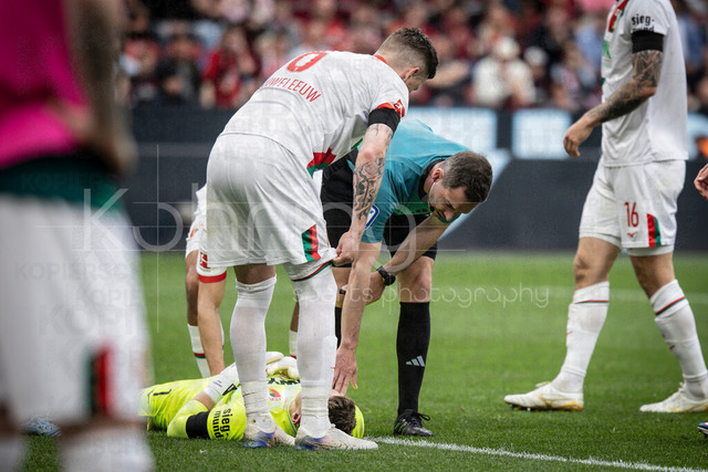German Bundesliga, Bayer 04 Leverkusen vs. FC Augsburg, 18.04.2026 | LEVERKUSEN, GERMANY - APRIL 18, 2026 :  Referee Benjamin Brand (Schwebheim) looks after injured Keeper Finn Dahmen (FC Augsburg, 1) during the German Bundesliga match on gameday 30 between Bayer 04 Leverkusen vs. FC Augsburg at BayArena on April 18, 2026 in Leverkusen, Germany. DFL REGULATIONS PROHIBIT ANY USE OF PHOTOGRAPHS AS IMAGE SEQUENCES AND/OR QUASI-VIDEO.