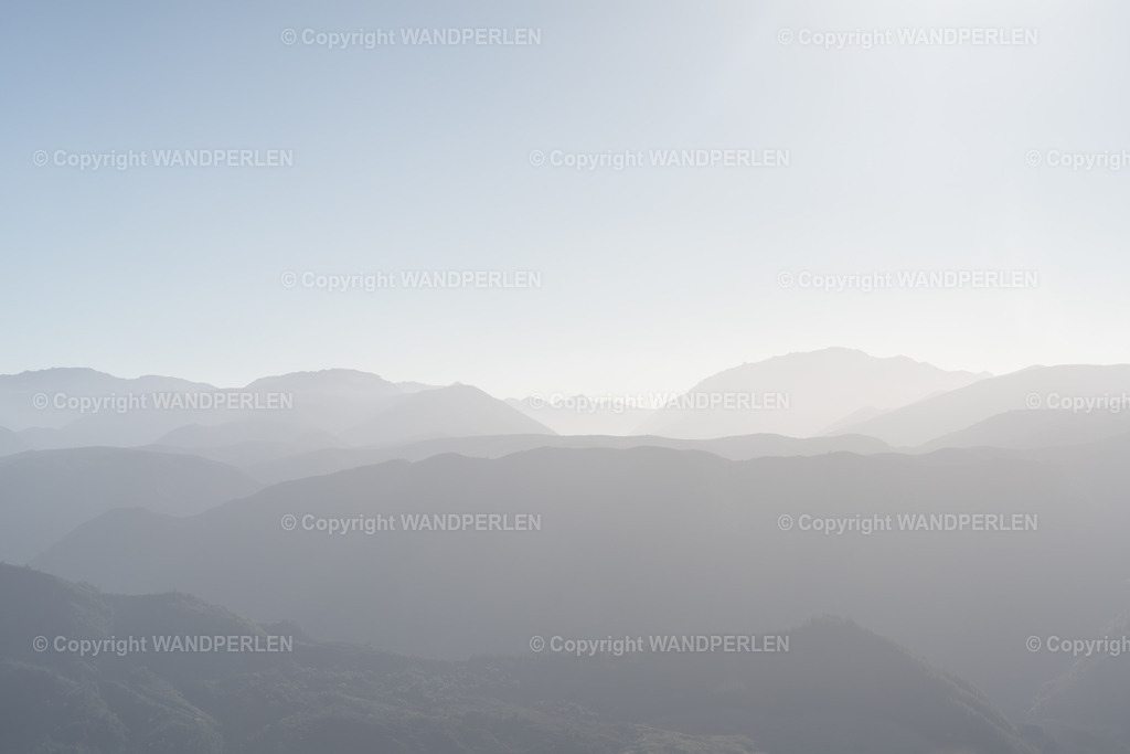 Abel Tasman – Abendliche Bergsilhouette / Abel Tasman - Mountain silhouettes in the evening | Abendlicht im Abel-Tasman-Nationalpark, Neuseeland – sanftes Sonnenlicht taucht die nebelverhangenen Berge in einen Schimmer und schafft eine traumhafte Landschaft aus Gipfeln und Tälern. Ein friedvoller Moment, eingefangen bei Sonnenuntergang. - Realisiert mit Pictrs.com