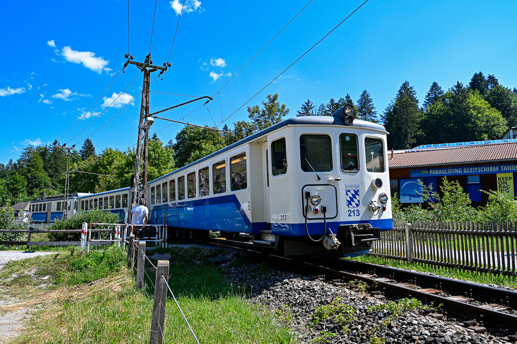 Mit Schwung in die Berge | Ein Hauch von Nostalgie und Vorfreude liegt in der Luft: Die blau-weiße Zahnradbahn Schlucht auf Schienen bahnt sich ihren Weg durch das idyllische Alpenvorland. Unter strahlend blauem Sommerhimmel verspricht die Fahrt eine Auszeit vom Alltag und weckt Erinnerungen an unbeschwerte Ausflüge, atemberaubende Panoramaaussichten und die Faszination klassischer Eisenbahnromantik. Ein Bild voller Reisefieber und Entdeckerlust! - Realisiert mit Pictrs.com
