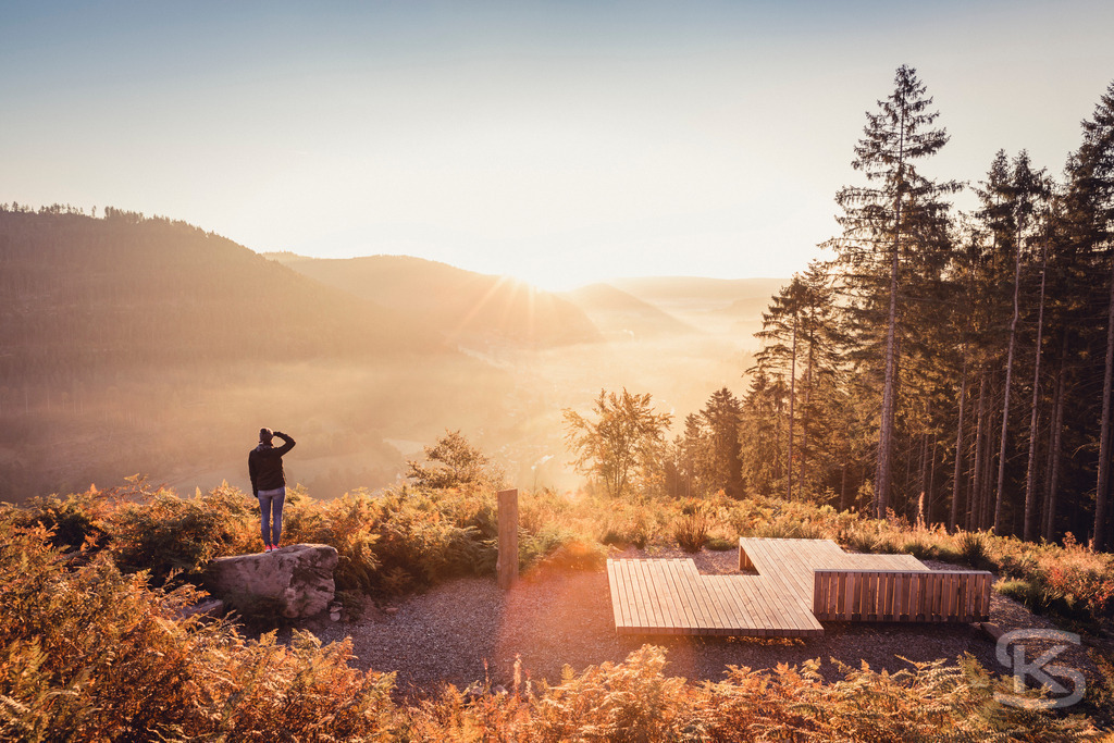 Sonnenaufgang am Genussplatz Oberer Zinken in Baiersbronn | Genießen Sie den traumhaften Ausblick vom Genussplatz Oberer Zinken in Baiersbronn, Baden-Württemberg. Das Bild fängt die stimmungsvolle Morgensonne ein, die das Tonbachtal in ein warmes Licht taucht und Nebel in den Tälern aufsteigen lässt. Ein perfekter Ort zum Entspannen, Verweilen und Genießen der Natur im Schwarzwald. - Realisiert mit Pictrs.com